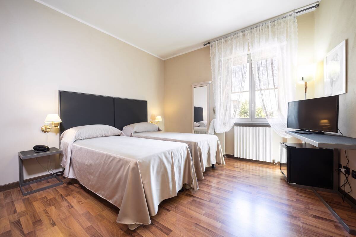A hotel room with two beds, a TV, a desk, and a window with curtains.