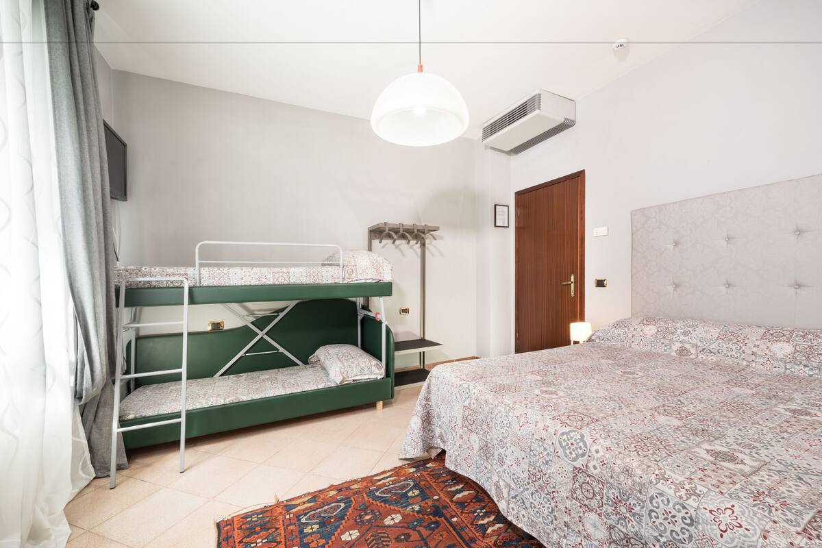 A room with bunk beds, a single bed, a patterned rug, a ceiling light, and a door.