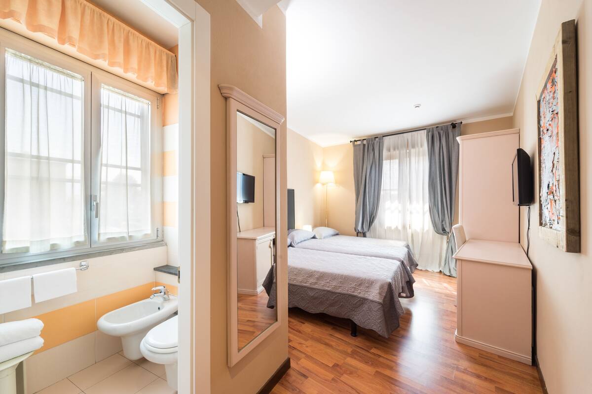 A hotel room with a bathroom, a bed, a TV, and a desk.