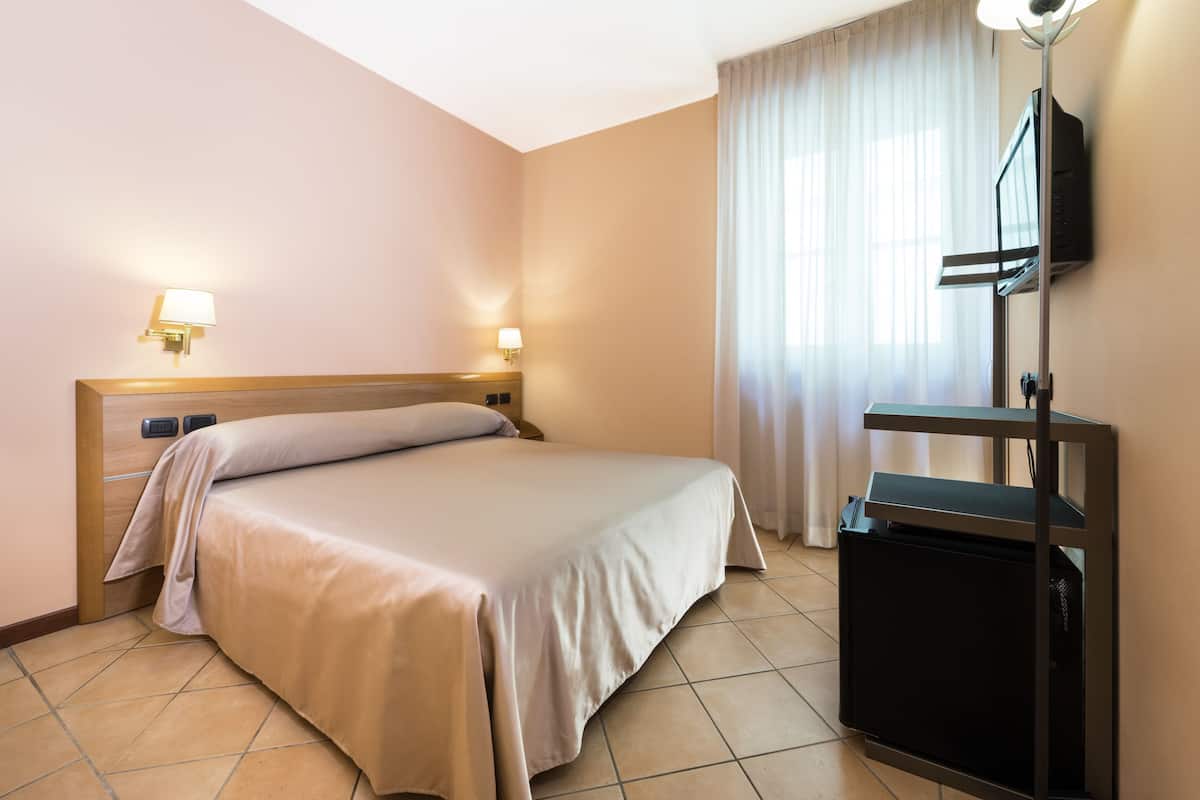 A hotel room with a bed, a TV on a stand, and two wall-mounted lamps.
