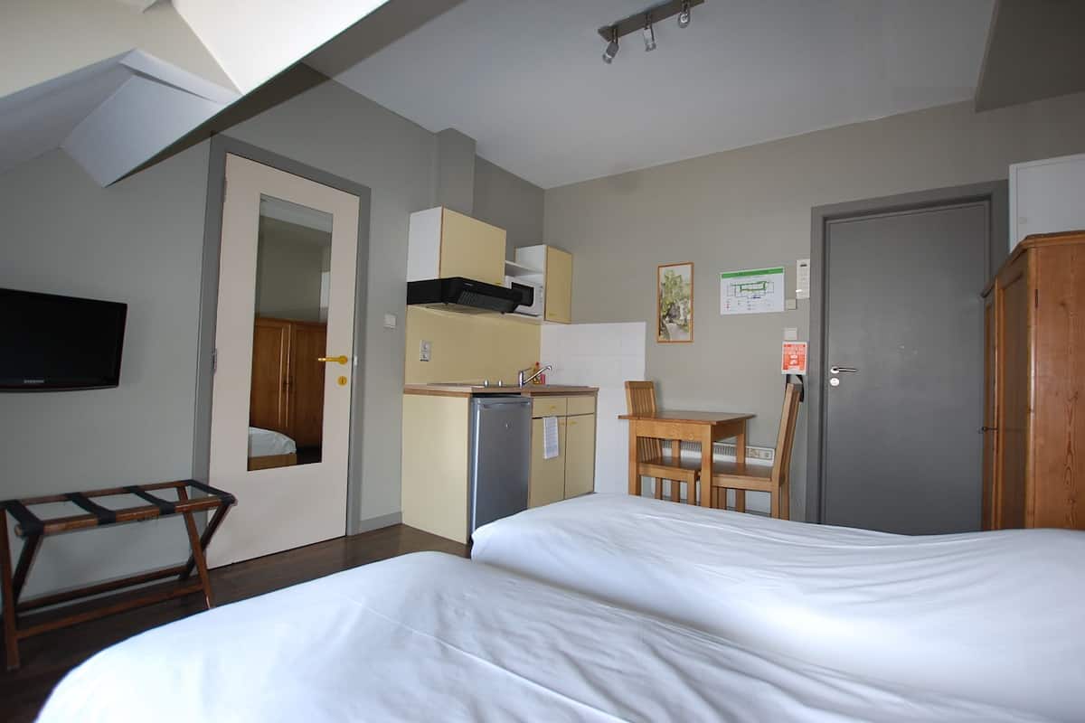 Una habitación de hotel con cama, escritorio, silla, kitchenette pequeña y televisión.