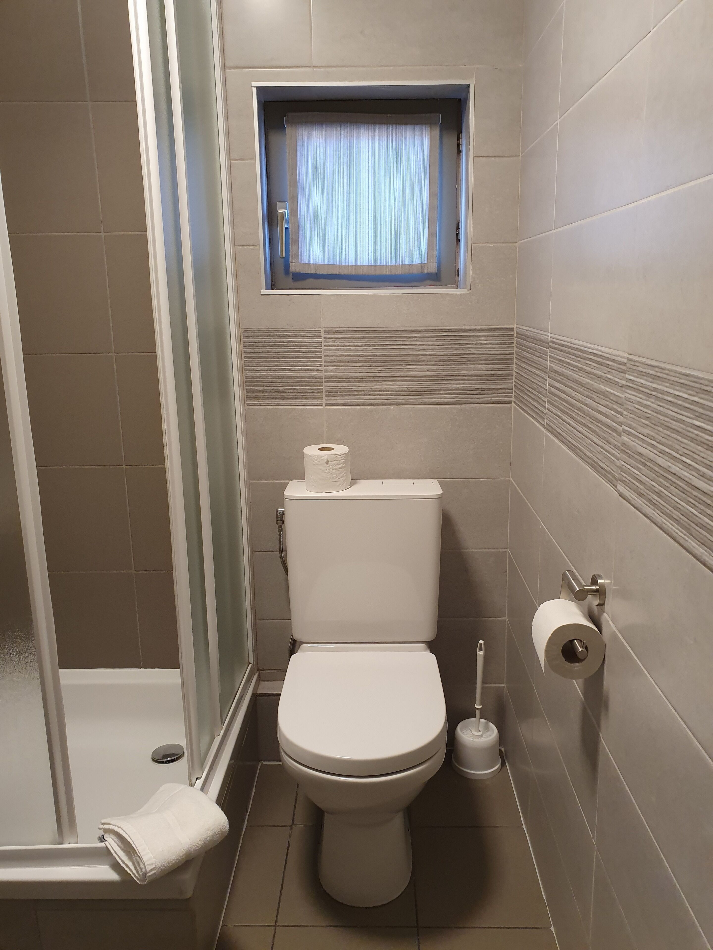 Une salle de bain comprenant des toilettes, une fenêtre avec des rideaux, une douche et un porte-serviettes.