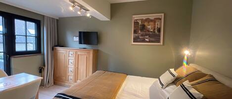A hotel room with a bed, a desk, a television, and a window.