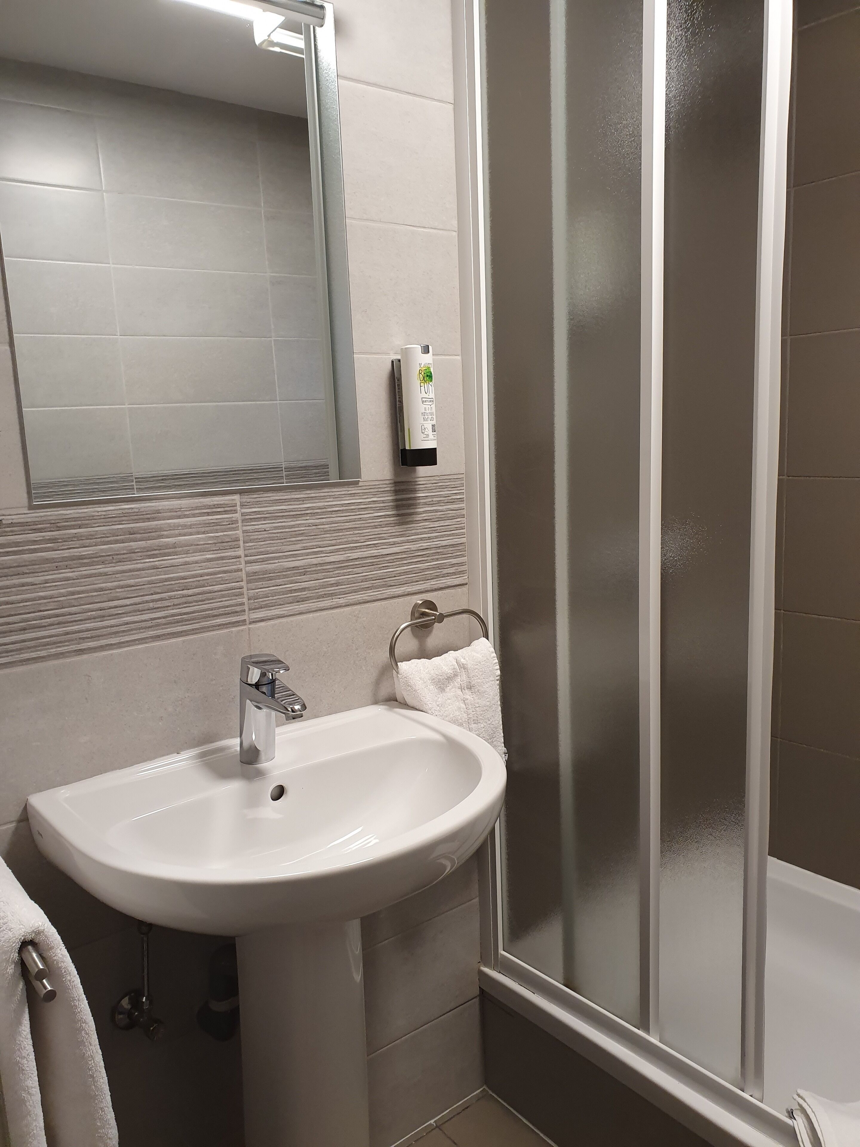 Une salle de bain avec un lavabo blanc, un miroir et une cabine de douche en verre.