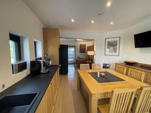 A modern kitchen with a dining area, wooden cabinets, a black refrigerator, and a flat-screen TV mounted on the wall.