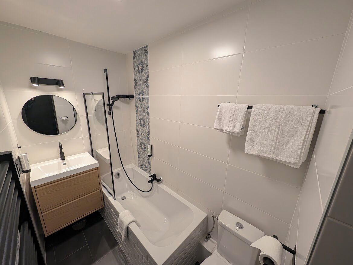 Une salle de bain moderne équipée d’une baignoire, de toilettes, d’un lavabo, d’un miroir et de deux serviettes posées sur un porte-serviettes.