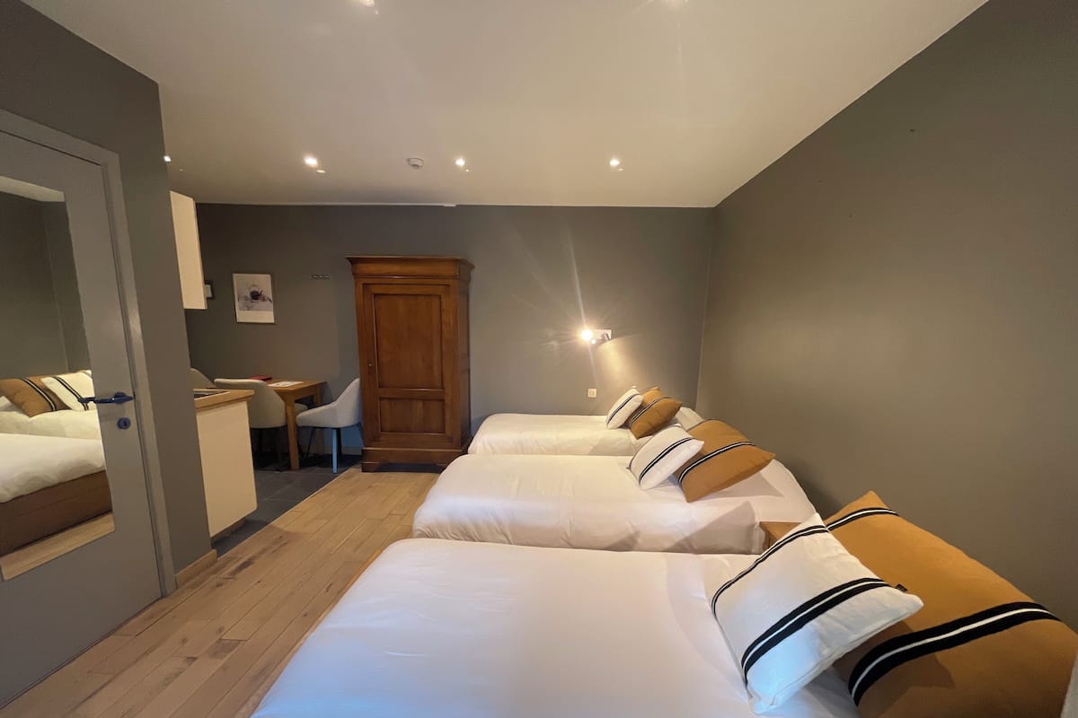 Habitación de hotel con piso de madera, un escritorio, una silla, un armario y dos camas con sábanas blancas y almohadas a rayas.