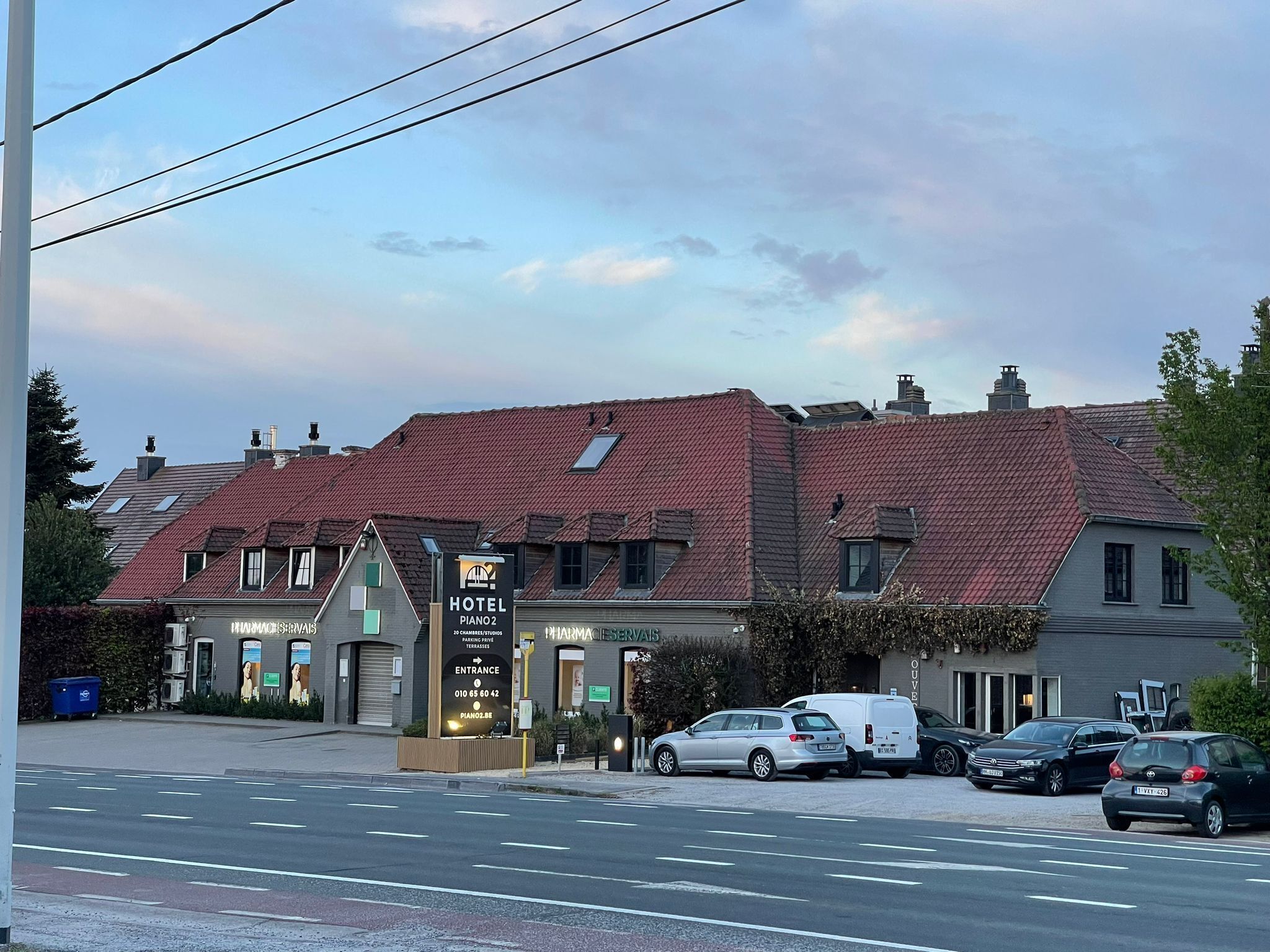 A hotel with a red-tiled roof, a signboard for the hotel, and several parked cars.