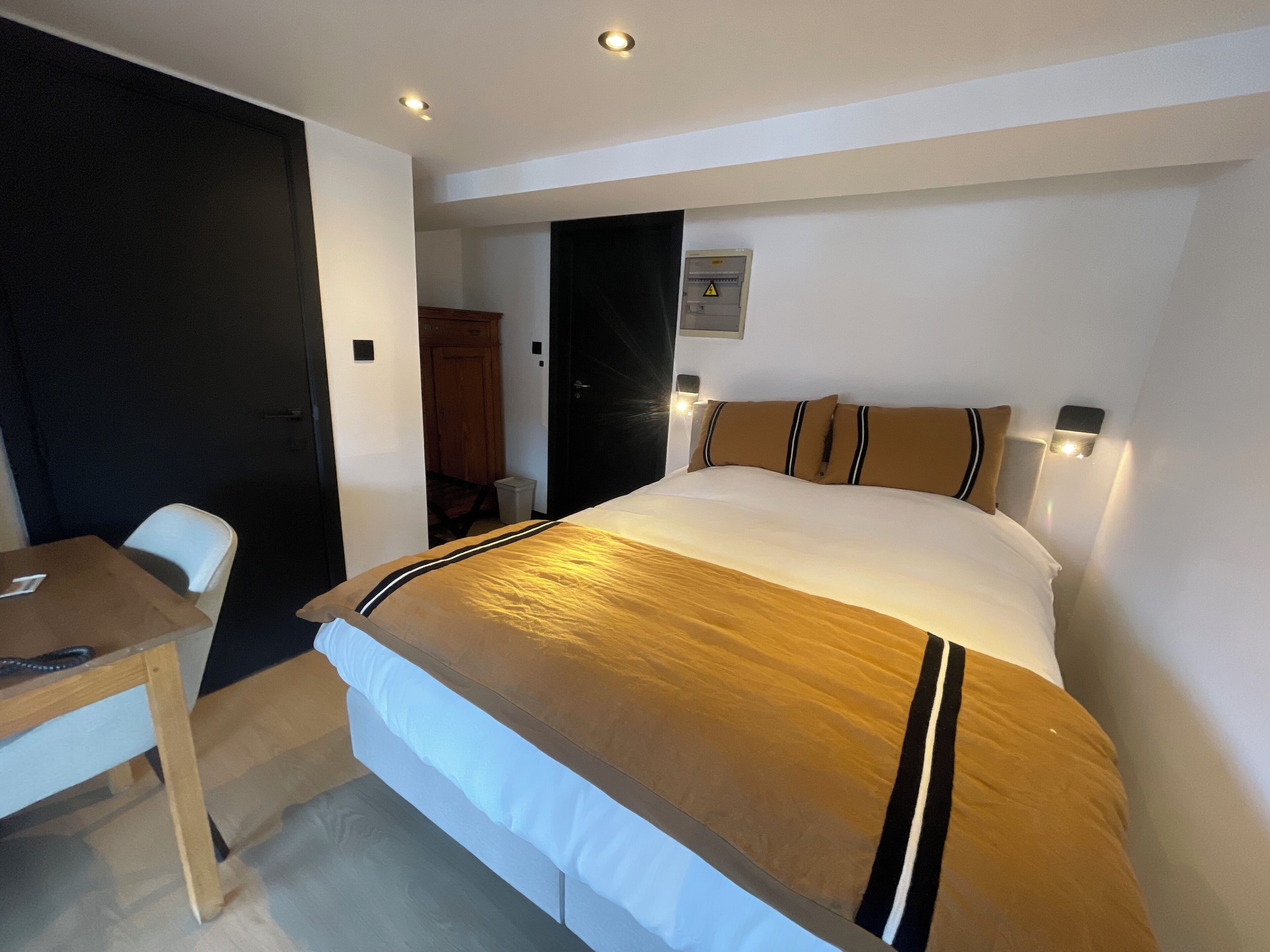A hotel room with a bed, bedside table, and a desk.