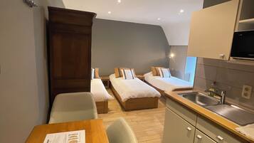 Habitación de hotel compacta con kitchenette, dos camas individuales, una mesa de comedor y un pequeño rincón de estar.