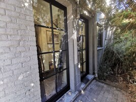 Un edificio con fachada de ladrillo, amplias ventanas y un pequeño espacio exterior con escalones que conducen a una puerta.