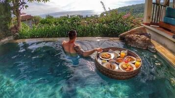 Un hombre en una piscina transparente con una cesta flotante de comida.
