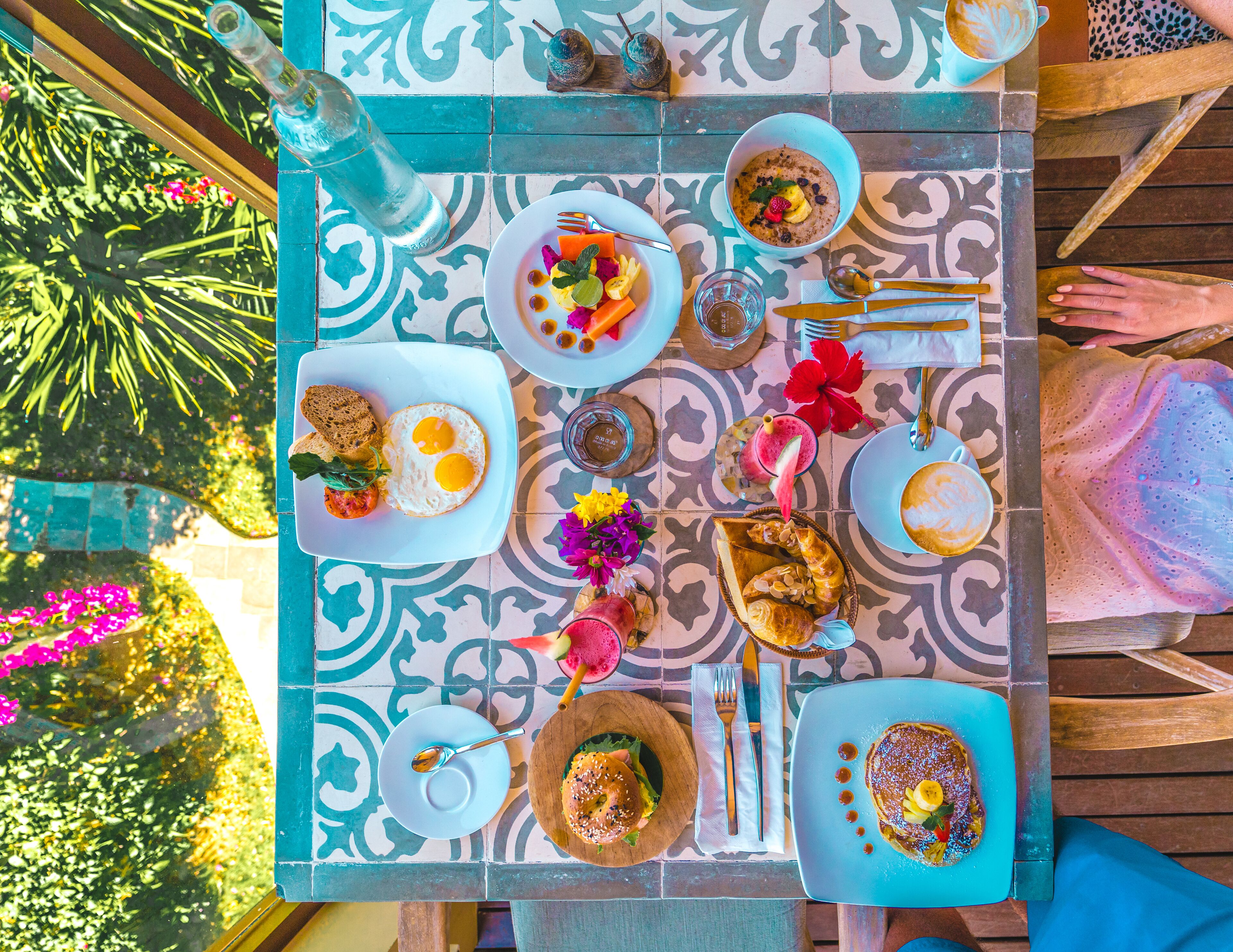 A dining table with various dishes, including pancakes, eggs, and a salad, set on a patterned tile floor.