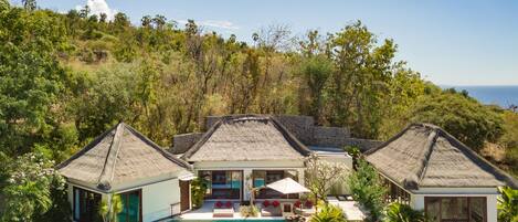 A resort with a pool, thatched-roof buildings, and a view of the sea.