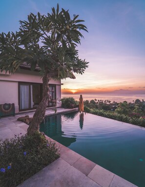 Una casa moderna con piscina, un árbol y vista al atardecer sobre el océano.