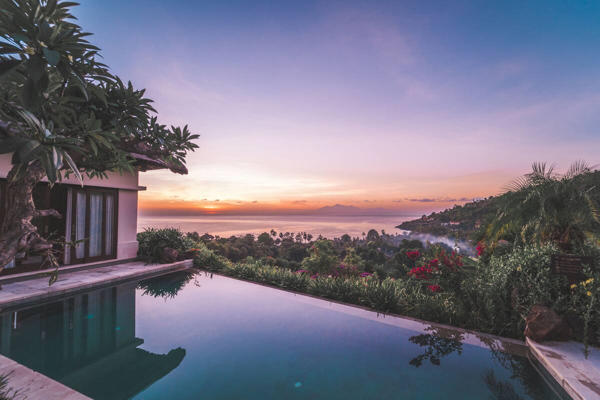 Una piscina infinita moderna con vista al océano al atardecer.