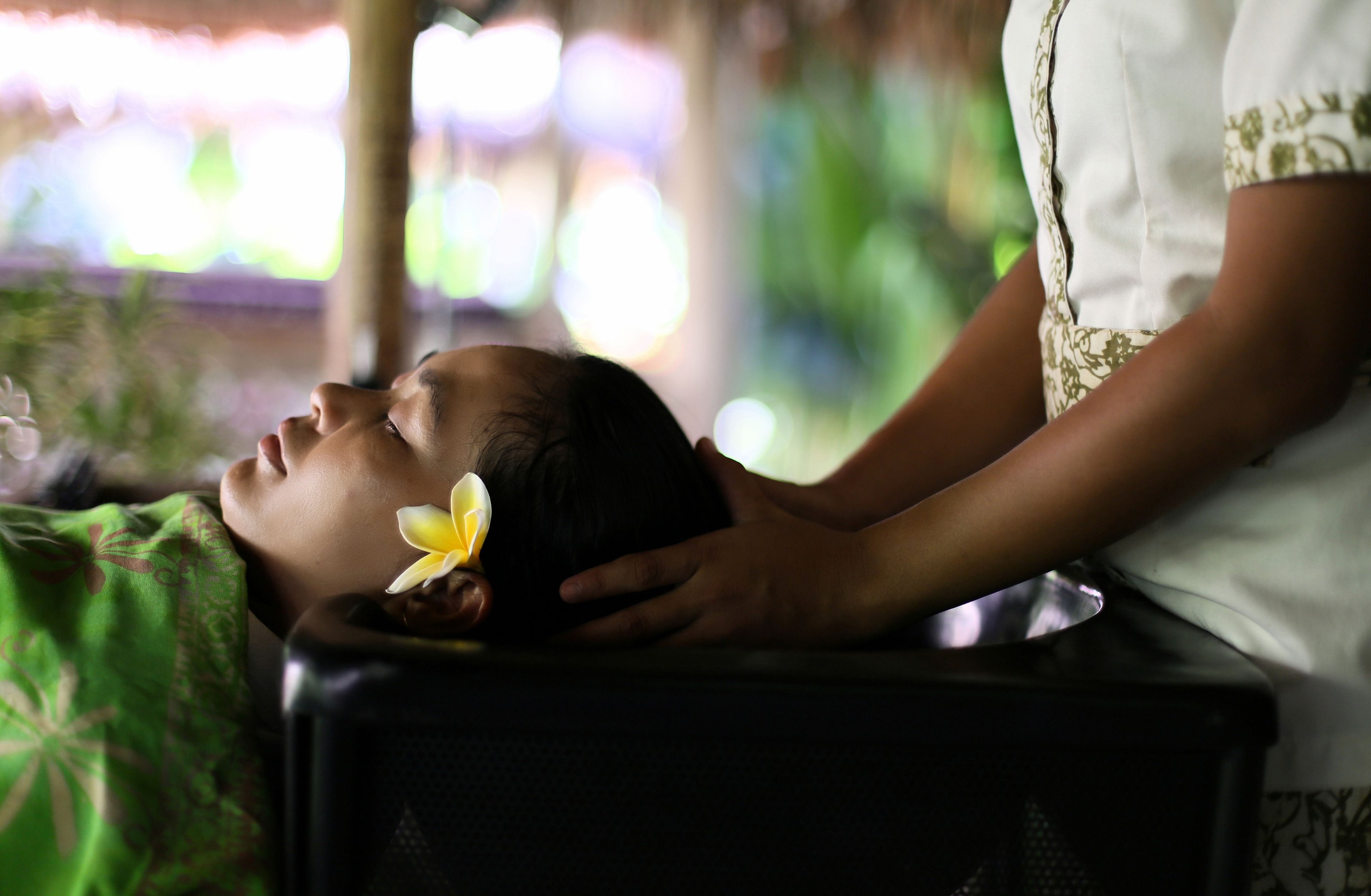 A person receiving a massage in a room with a green patterned blanket and a flower on their head.
