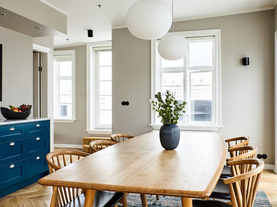 Un comedor con una mesa de madera, armarios azules y un jarrón con flores.