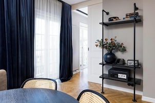 Una sala de estar moderna con una mesa de comedor, sillas, un mueble negro para entretenimiento y un amplio ventanal con cortinas.