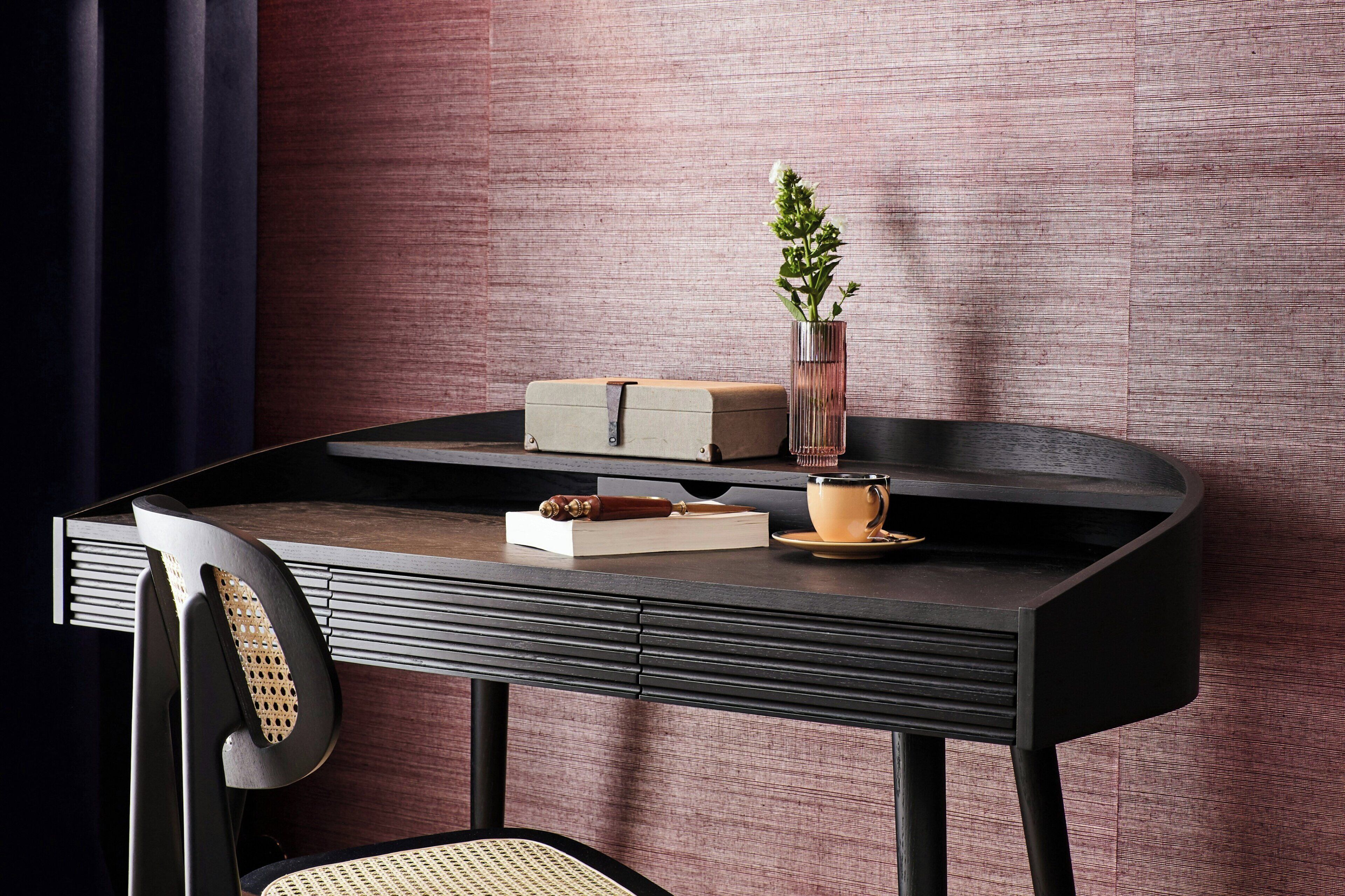 A modern, dark-colored desk with a vase of green plants, a book, and a cup.