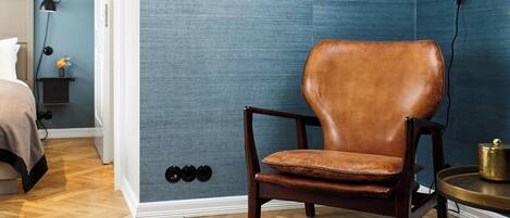 A room with a wooden floor, a brown leather chair, a small round table with a brass object, and a blue textured wall.