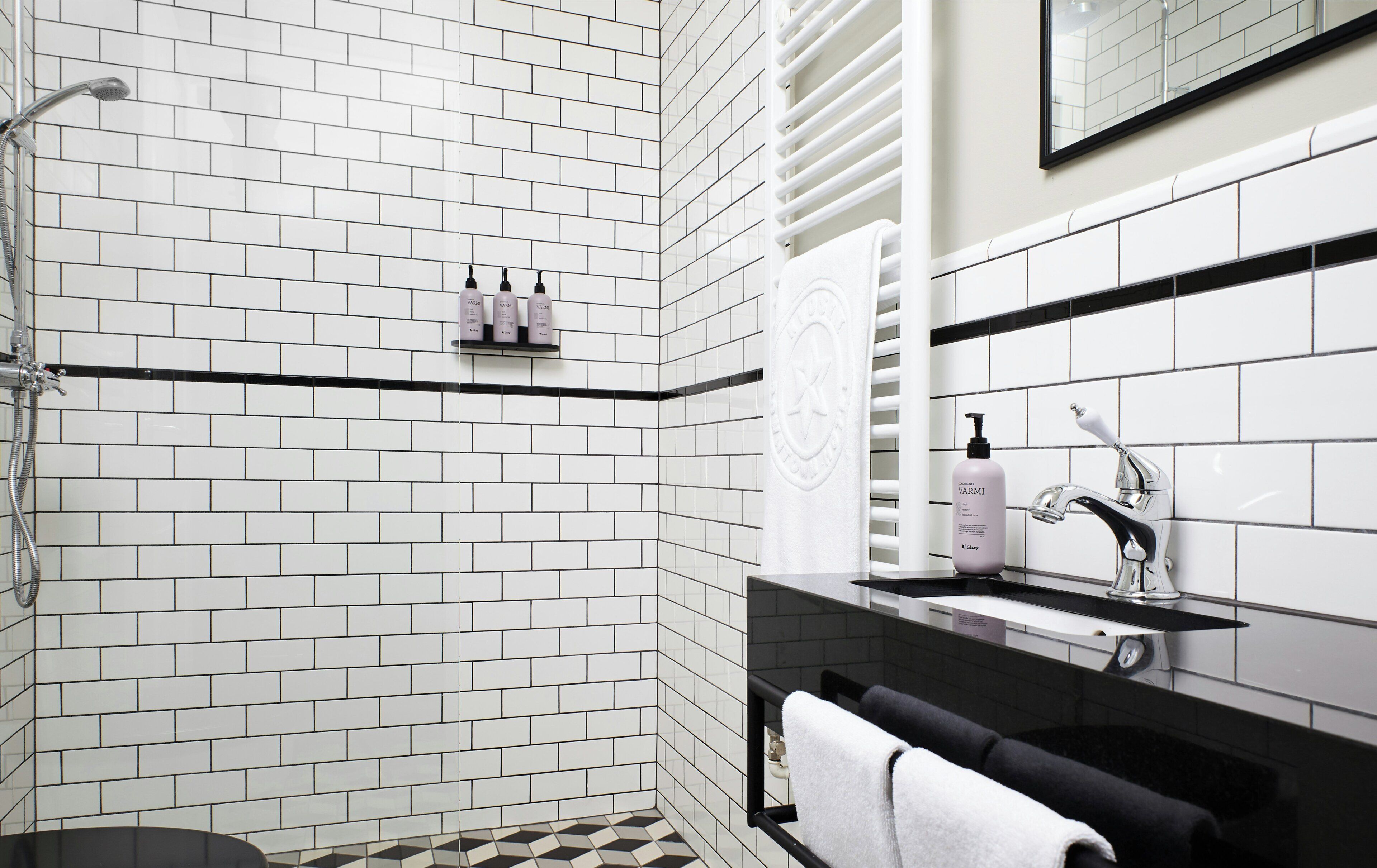 A bathroom with white subway tiles, a shower with a handheld showerhead, a vanity with a mirror, and a towel rack.
