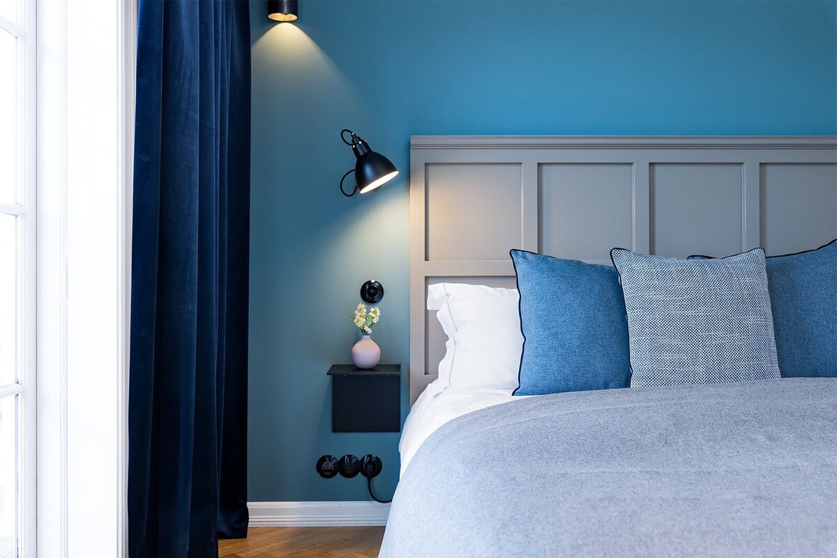 Une chambre à coucher comprenant un lit, une table de chevet, une lampe et une prise de courant fixée au mur.