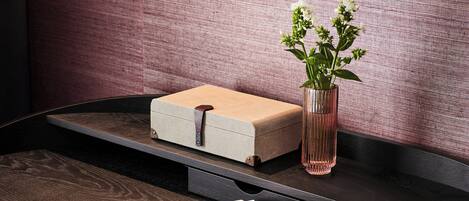 A wooden table with a white box, a magnifying glass, a book, a vase with flowers, and a cup of coffee.