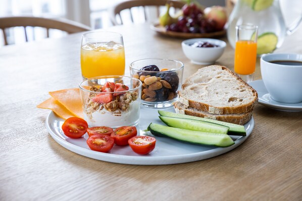 A breakfast tray with yogurt, almonds, tomatoes, cucumber slices, and bread on a wooden table.