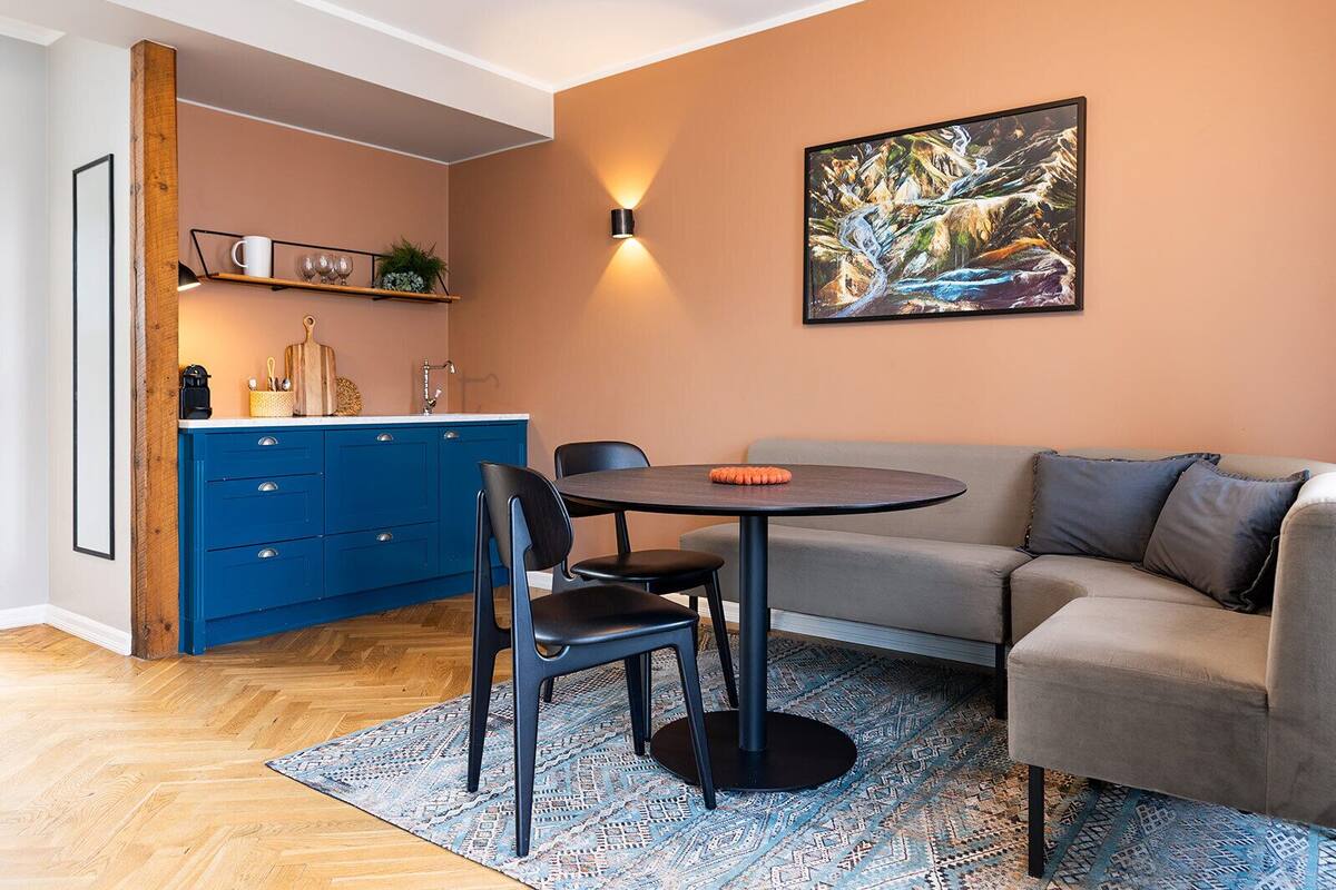 Un salon chaleureux avec une cuisine bleue, une table ronde et un canapé gris.