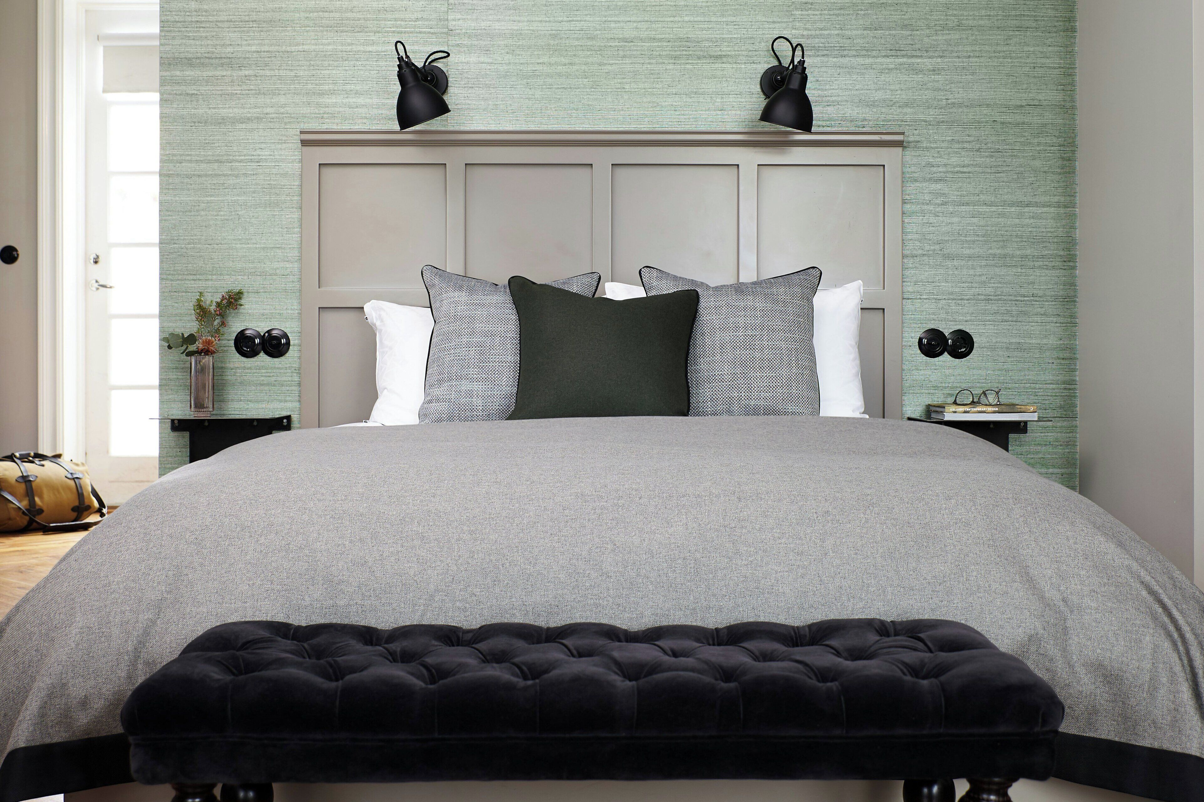 Una cama con edredón gris, cabecera negra y un banco tapizado negro.