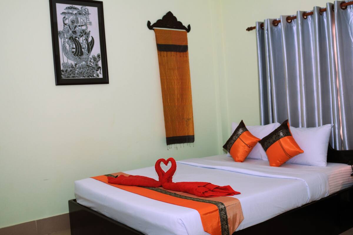 Una cama bien hecha con ropa de cama naranja y blanca, una toalla con forma de corazón y dos almohadas naranjas.