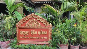 A sign for the Popular Boutique Hotel surrounded by lush greenery and potted plants. - Popular Boutique Hotel (Siem Reap)