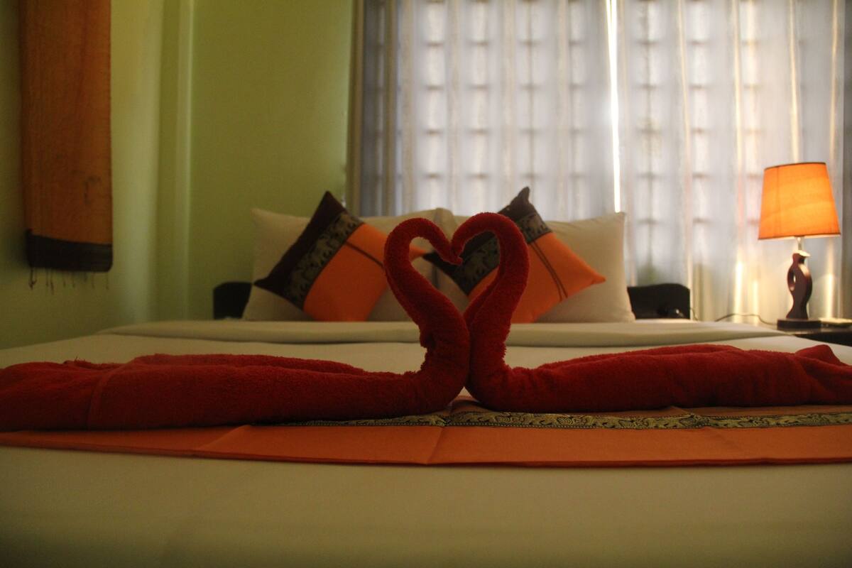 Una habitación de hotel con una cama bien hecha, almohadas, una lámpara y una ventana con cortinas.