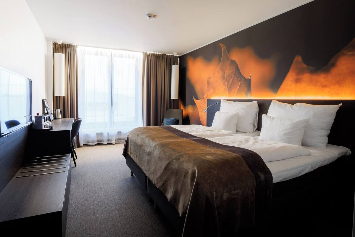 A hotel room with a bed, a desk, and a large window.