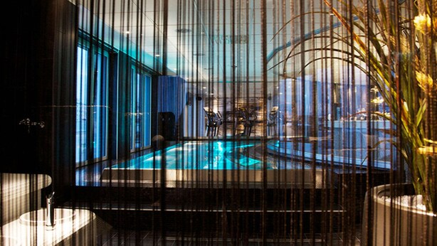Zona de piscina interior moderna con vistas a la ciudad a través de amplias ventanas.