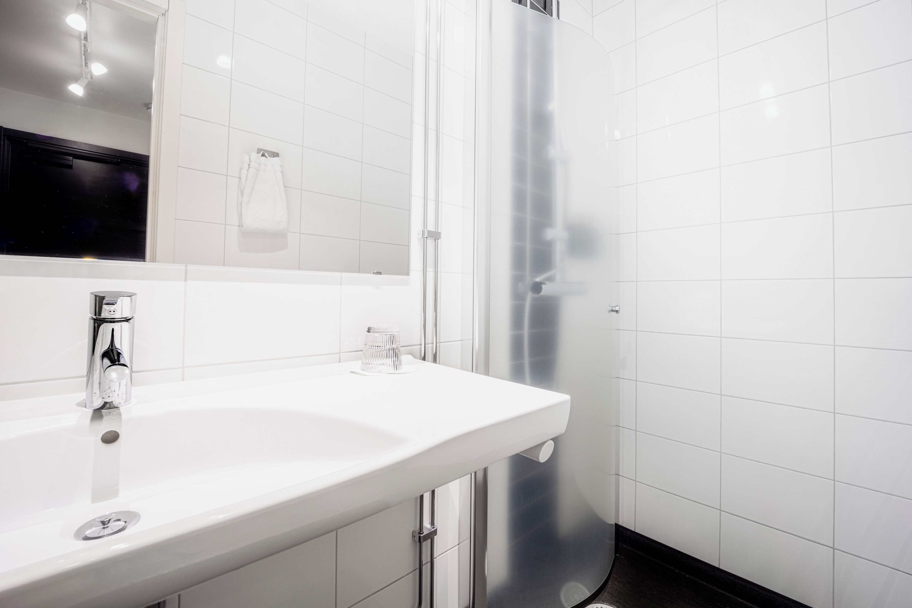 A modern bathroom with a white sink, a mirror, and a glass shower enclosure.