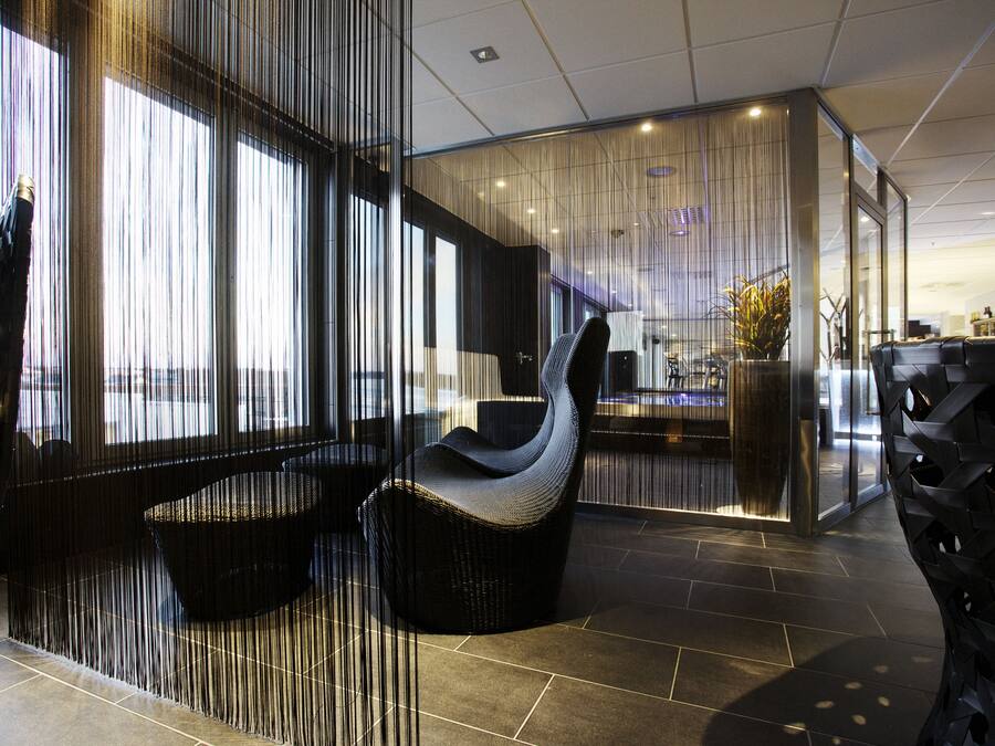 A modern interior with a curved black chair, a glass partition, and a tiled floor.