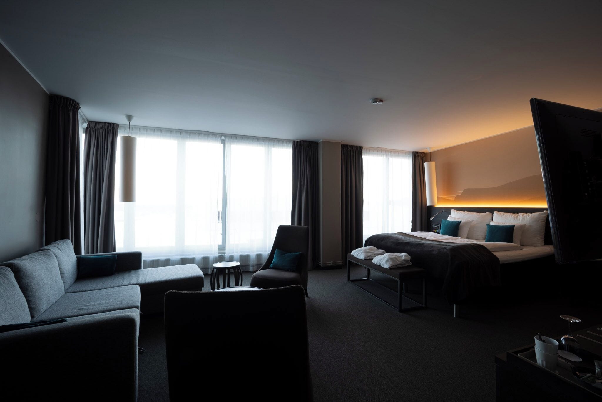 A hotel room with a sofa, armchair, a small round table, a bed with pillows, and a TV.