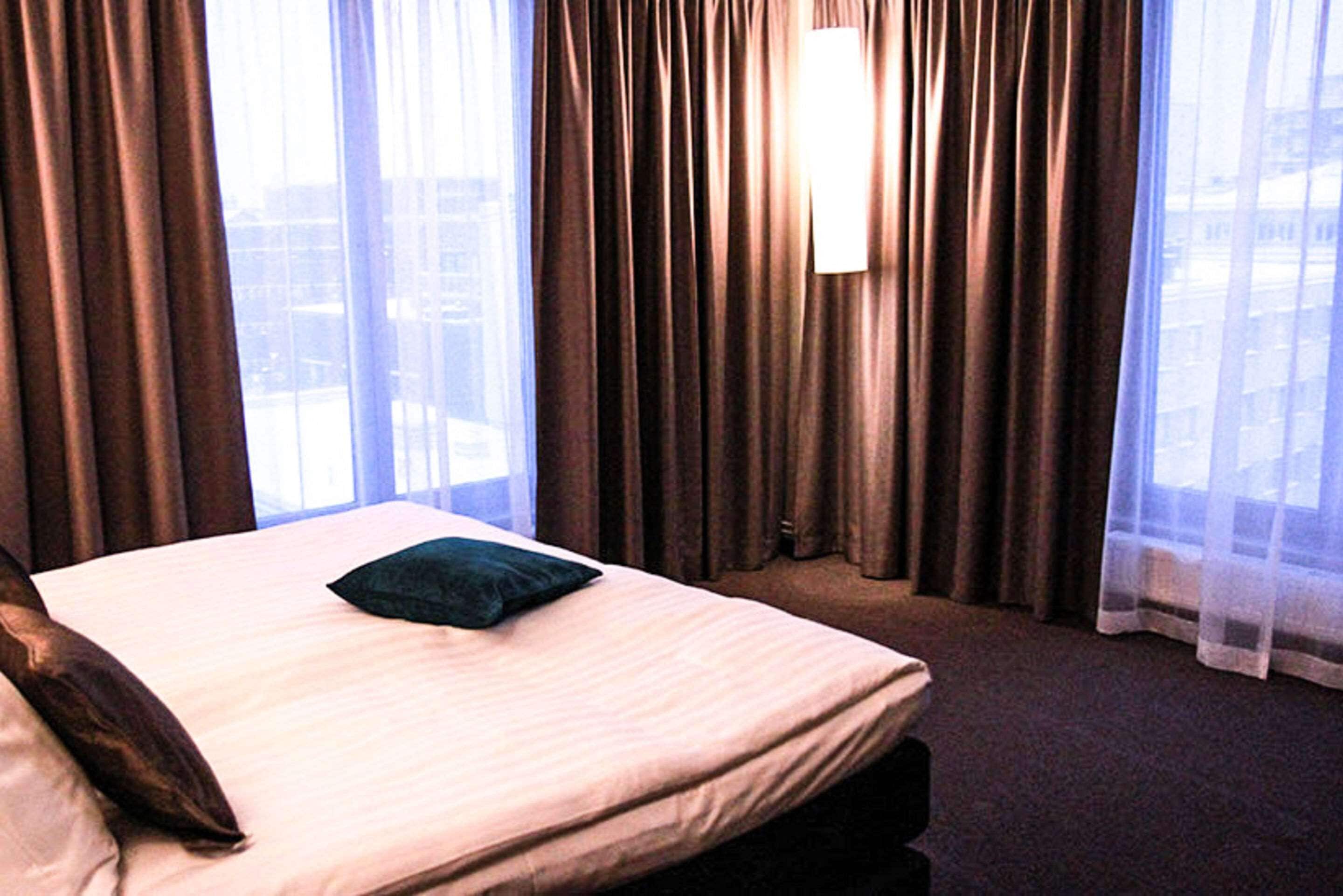 Ein Hotelzimmer mit Bett, Vorhängen und Blick auf Gebäude durch das Fenster.