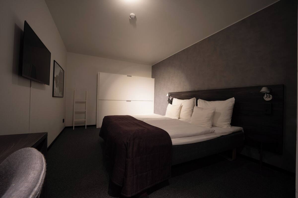 A modern hotel room with a large bed, a flat-screen TV, a desk, and a chair.