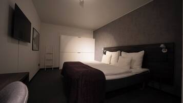 Quarto de hotel moderno com uma cama grande, televisão de tela plana, escrivaninha e uma cadeira.