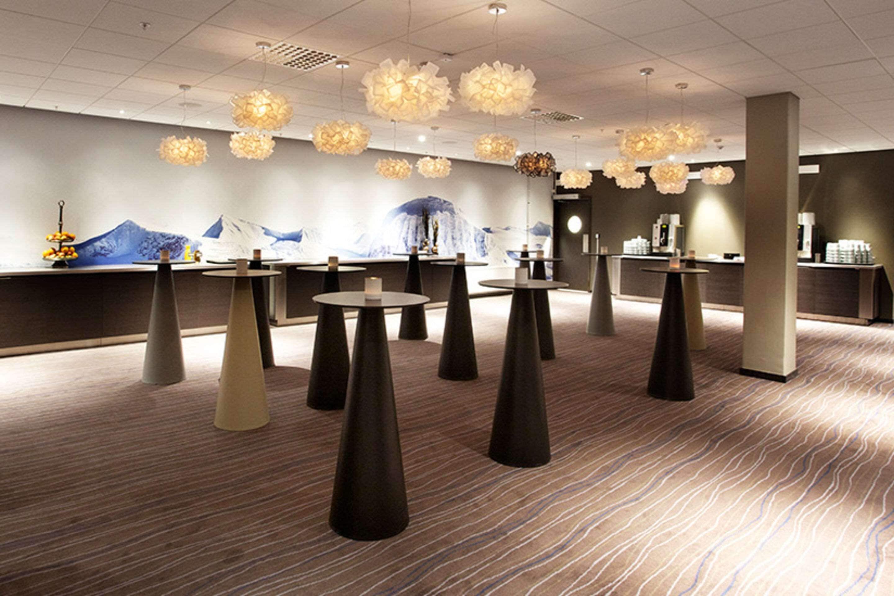 A modern hotel lobby with round tables, a reception desk, and decorative lighting.