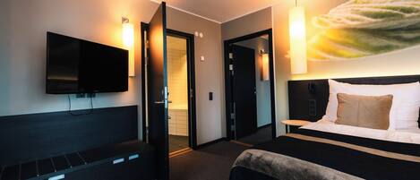 A hotel room with a bed, a TV, a bench, and a painting on the wall.