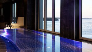 Un área de piscina interior moderna con vistas a una masa de agua a través de amplias ventanas.