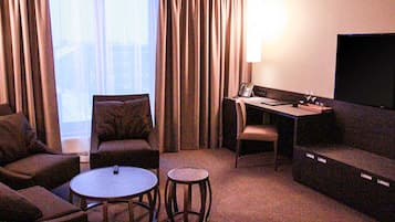 A hotel room with a sofa, two armchairs, a small round table, a desk with a chair, and a flat-screen TV.