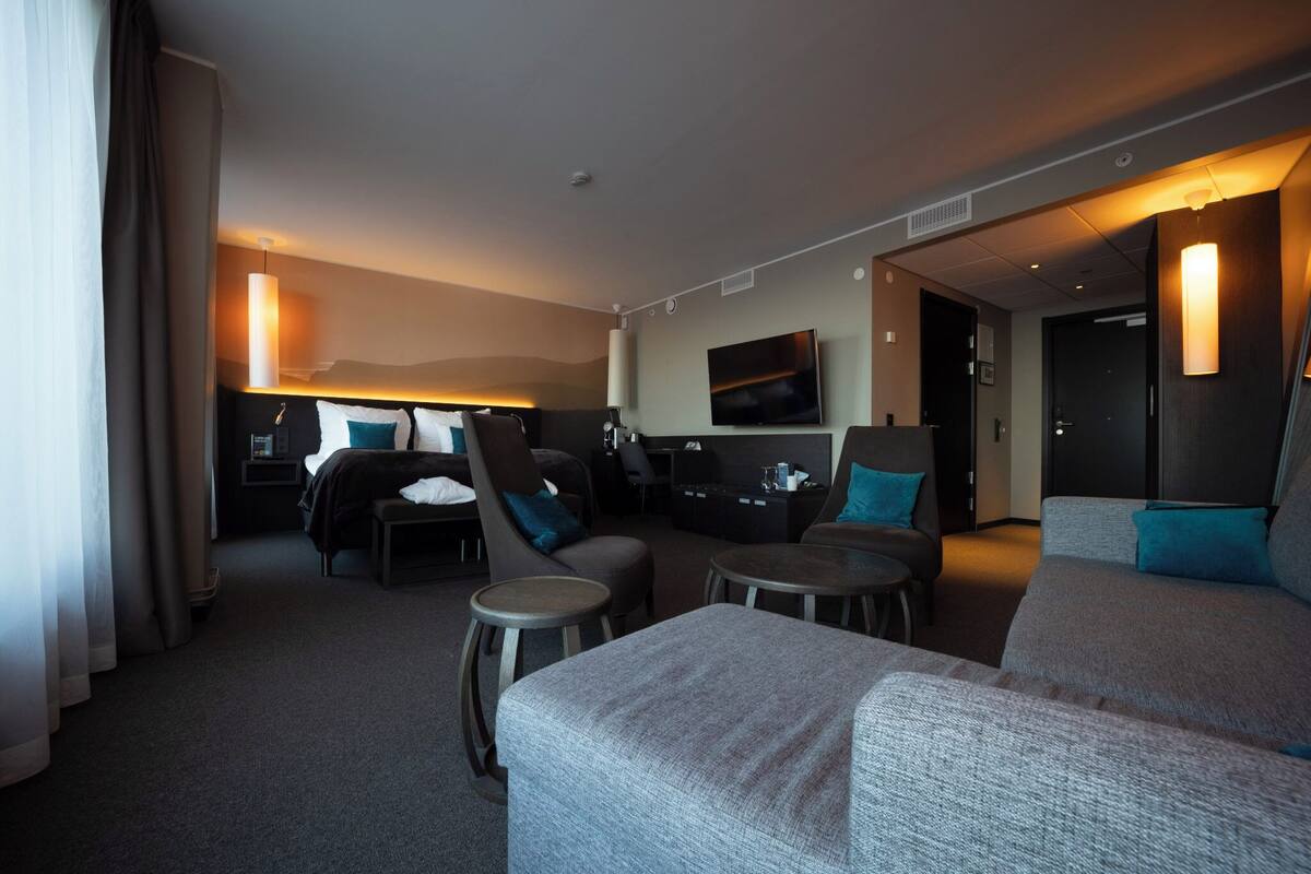 A modern hotel room with a large bed, a sofa, a desk, and a television.