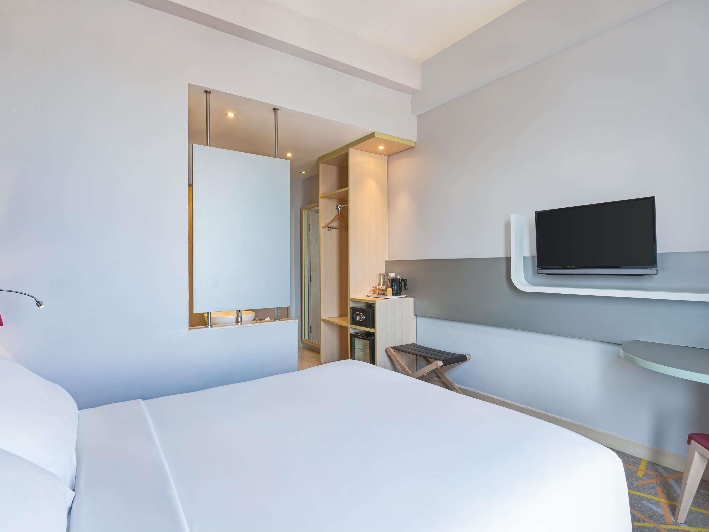 Hotelkamer met een bed, een aan de muur bevestigde televisie, een bureau met stoel en een spiegel.