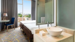 A hotel room with a bed, a desk, a chair, a large mirror, and a bathroom with a sink and toilet. - Ibis Styles Malang (Malang)