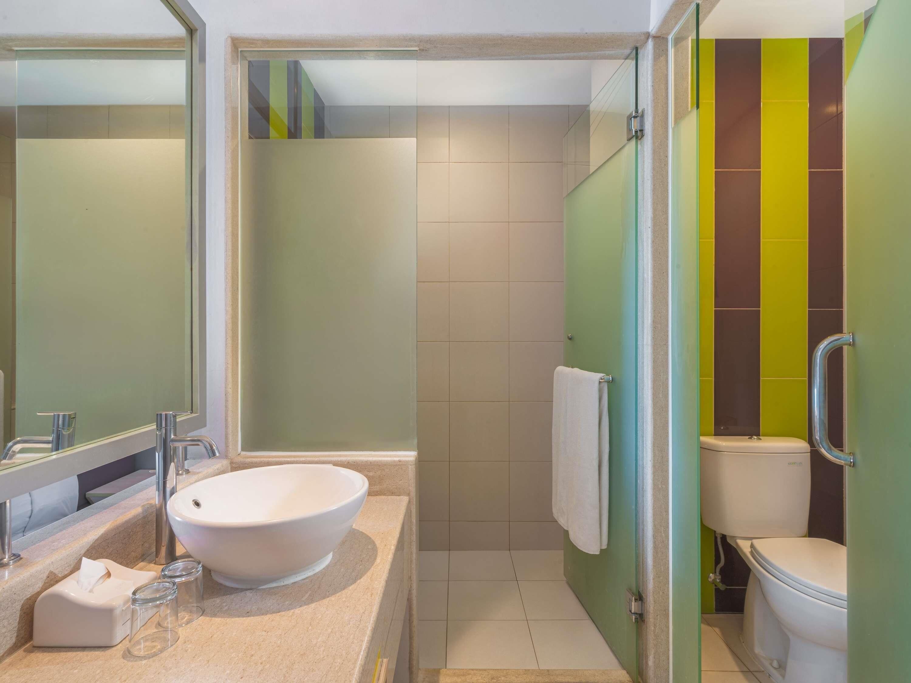 A bathroom with a large mirror, a sink with a bowl, a glass shower enclosure, and a toilet.